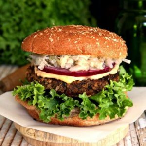 Crispy Anasazi Bean Burger is perfectly centered for the photo and has latyers of curly green lettuce, crispy brown burger, white sauce, red onion and sauerkraut. All is covered with a bun top.