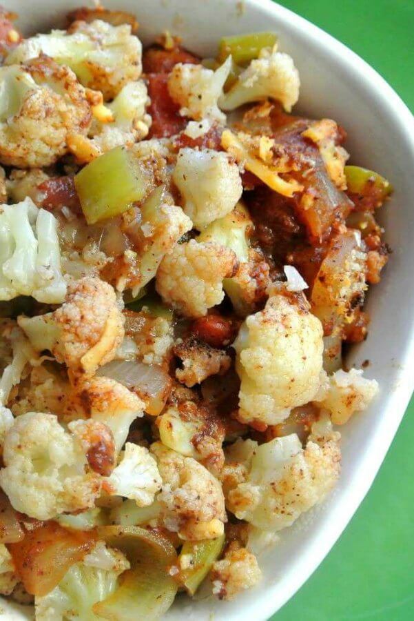 Mexican Cauliflower Casserole is piled high in a white bowl with a green background.It's a super close-up photo of golden herbs and veggies.