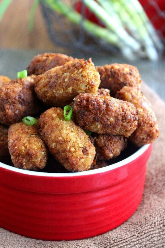 Vegan Chickpea Cauliflower Tots are golden brown logs and piled high in a red bowl. Close up photo to show the perfect tots.