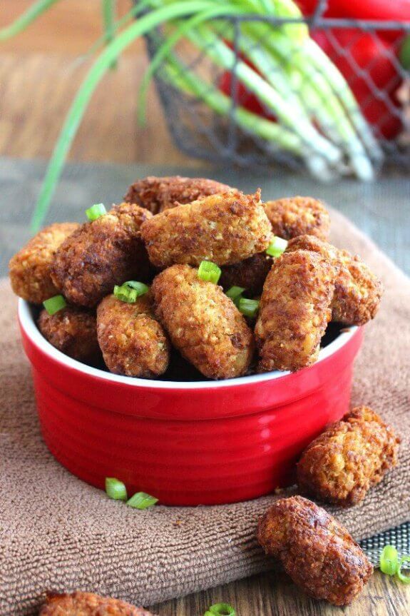 Vegan Chickpea Cauliflower Tots are fried up into crispy mini logs and piled high in a red serving bowl. Sprinkled with fresh snipped green onions.