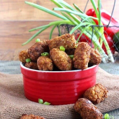 Vegan Chickpea Cauliflower Tots are golden brown and piled in a red bowl with red bell peppers and green onions in a basket behind.
