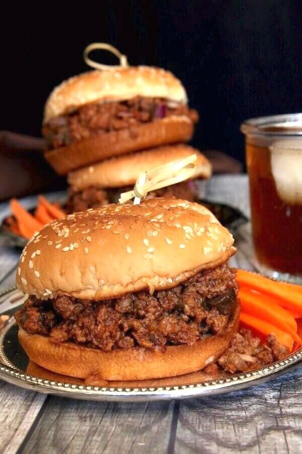 Vegan Sloppy Joes are overflowing with a spicy and tangy plant based filling rich in tangy mushrooms and onions. Bright orange carrot sticks are within reach.
