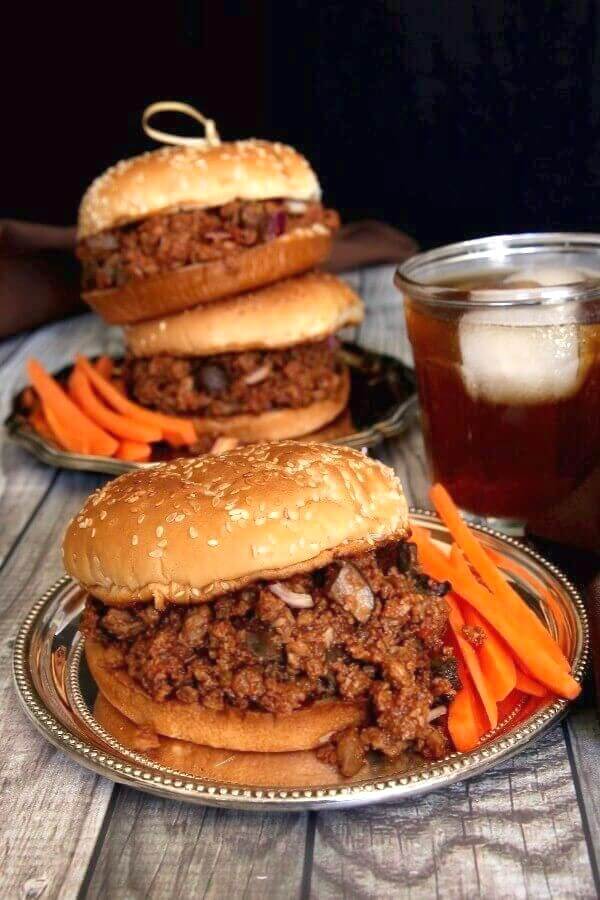 Vegan Sloppy Joes are overflowing with a spicy and tangy plant based filling all on to a silverplate server. Bright orange carrot sticks are within reach.