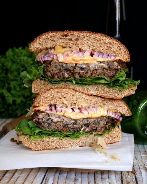 Crispy Anasazi Bean Burger have two halves stacked on top of each in this photo. Looking straight at the cross section of sliced patties, red onion and sauerkraut is begging for a bite.