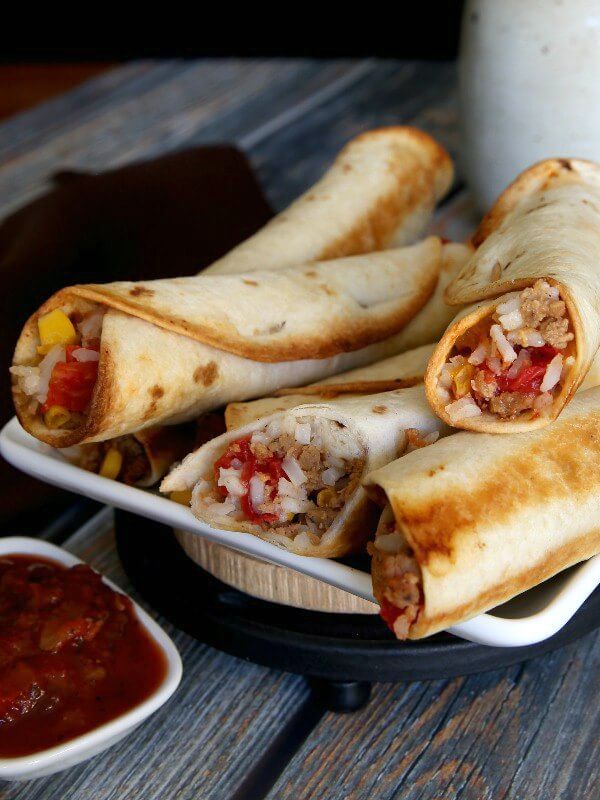 Vegan Rice and Beef Burrito piled high on a white square plate and angles in all directions. Some are cut in half to show the rich red, yellow, white and golden vegetables.