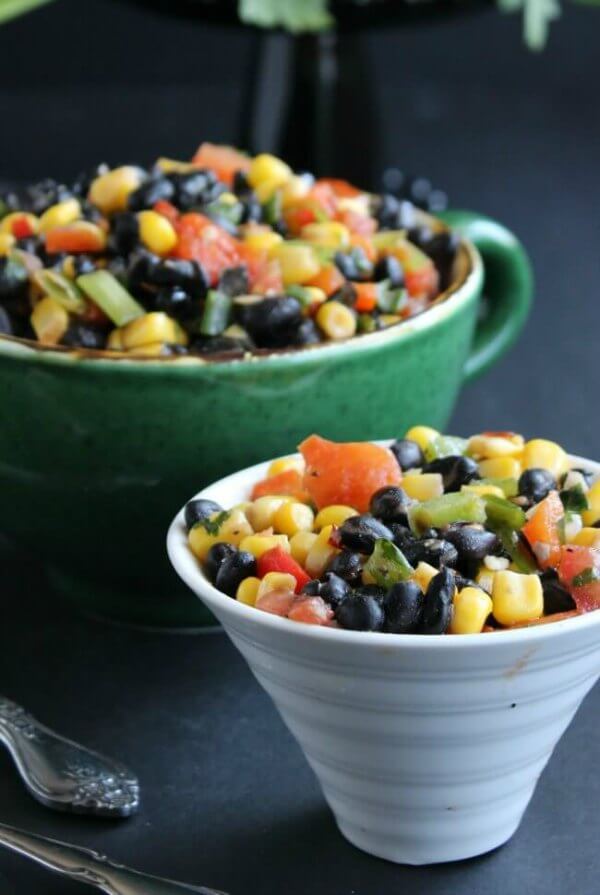 Fully Loaded Black Bean Salad is bright and inviting with yellow, black, orange and green and it's served in a giant green cup with a white flared bowl sitting in front.
