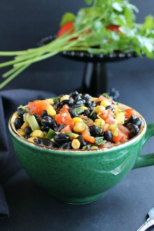 Fully Loaded Black Bean Salad is bright with yellow, black, orange and green and it's served in a giant green cup.