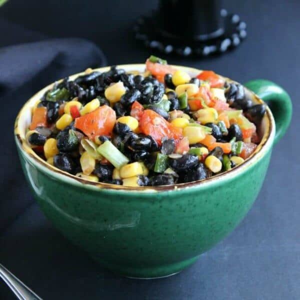 Fully Loaded Black Bean Salad is bright and inviting with yellow, black, orange and green and it's served in a giant green cup.