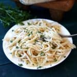 Vegan Chicken Tetrazzini Casserole is spaghetti that is covered with a rich white sauce. It's sitting on a white plate and is sprinkled with fresh tarragon.