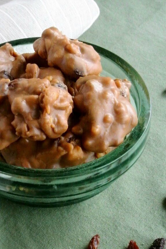 Black Walnut Pralines are light golden brown dollops of rich candy all sitting in a forest green glass bowl.