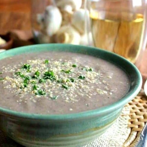 Best Creamy Mushroom Soup is filling w green stripped pottery bowl with vegan parmesan and parsley sprinkled on top.