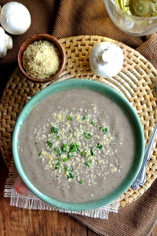 Best Creamy Mushroom Soup is filling w green stripped pottery bowl with vegan parmesan and parsley sprinkled on top. Looking down from overhead.