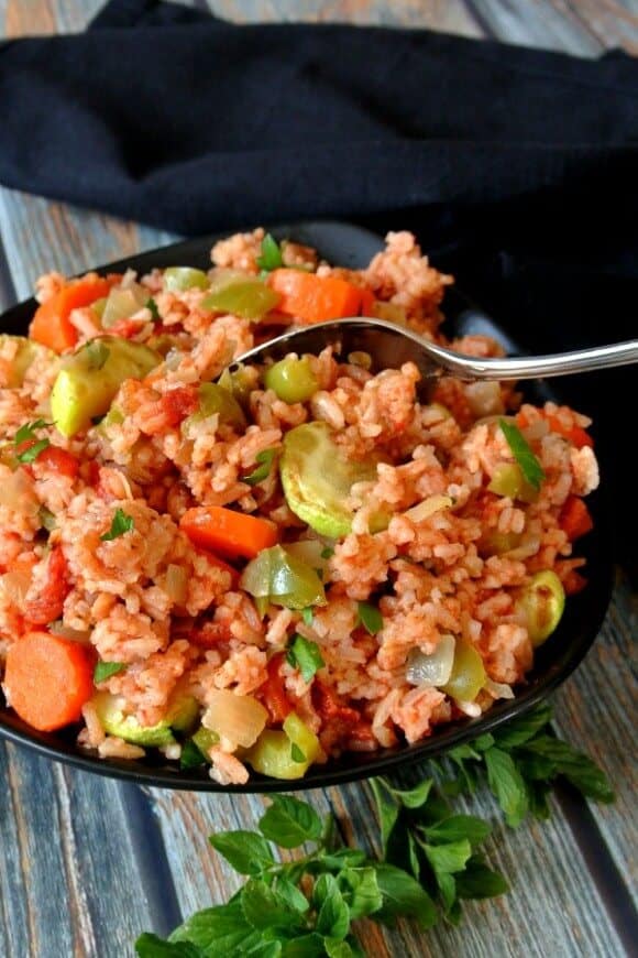 Garden Vegetable Rice Pilaf is is sharing a black bowl with green, red and orange vegetables. Sprinkled with fresh parsley.