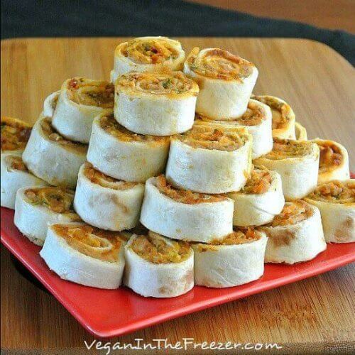 Pesto Tortilla Rollups are sliced into 1 1/2" rounds and are stacked like a pyramid. All are sitting on a red square plate.