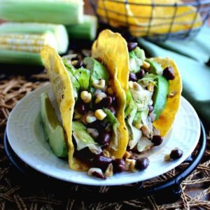 Corn and Black Bean Salsa Tacos are two to a plate and overflowing with green, yellow and black beans. White plate is sitting on a black trivet.