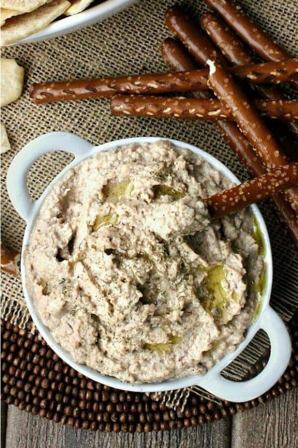 Best Kalamata Hummus is an overhead photo and looking down at piled high hummus in a flat handled bowl and drizzled with extra virgin olive oil and fresh herbs