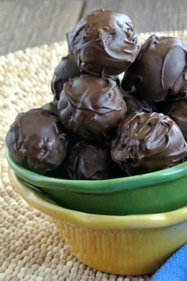 Peanut Butter Cups Balls are glistening chocolate balls piled in a green bowl and that bowl is sitting in a yellow one.