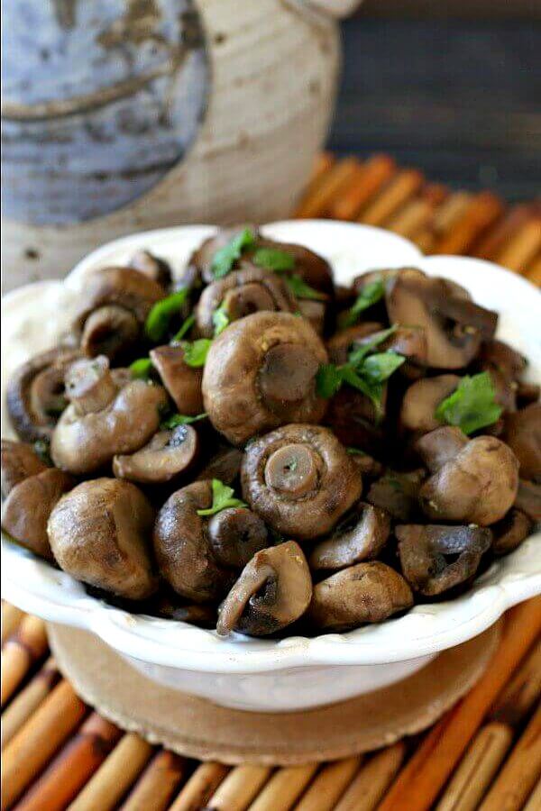 Healthy Slow Cooker Balsamic Glazed Mushrooms are in a while scalloped bowl sitting on cork coaster and bamboo mat.