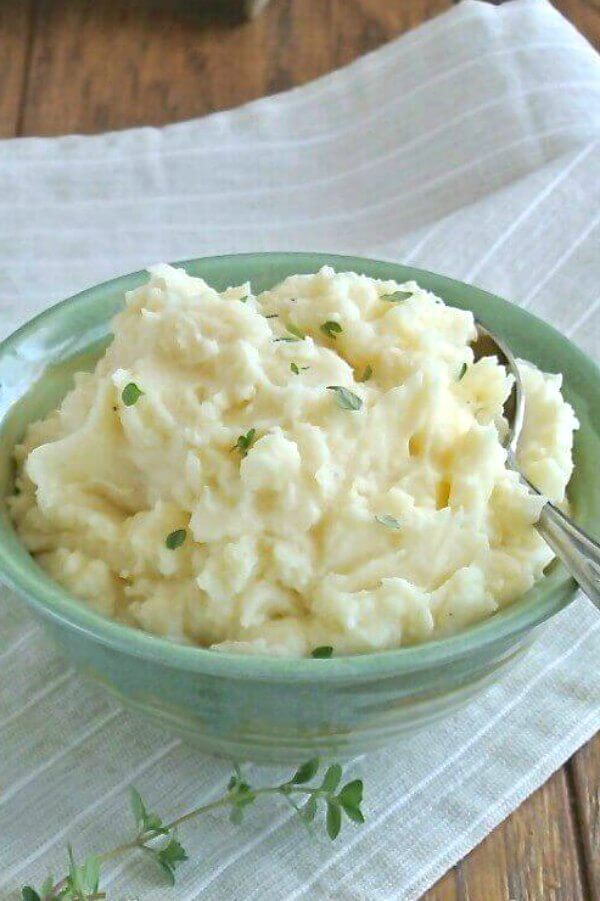 Creamy mashed potatoes are in a green bowl with thyme sprinkled on top.