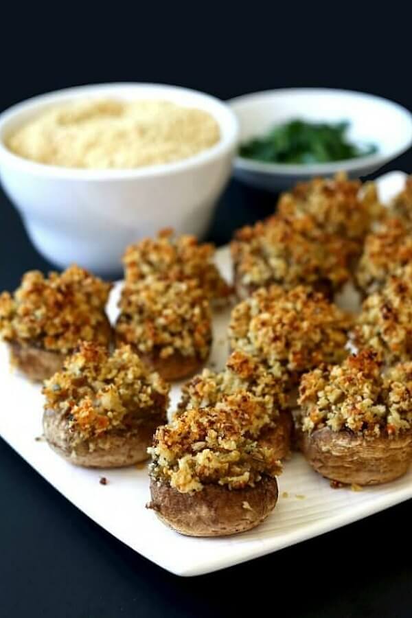 Vegan Holiday Stuffed Mushrooms lined up, without touching, on a rectangle white plate. Baked to a golden brown and ready for picking.