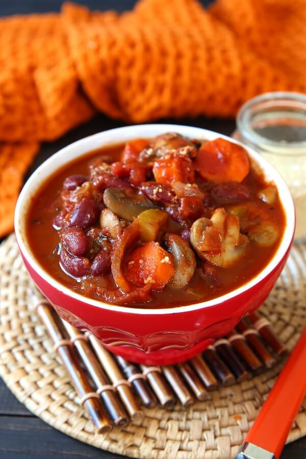 Best Vegan Chili Recipe with Mushrooms is tilted forward in a bright red bowl and has an orange handled spoon laying along side.