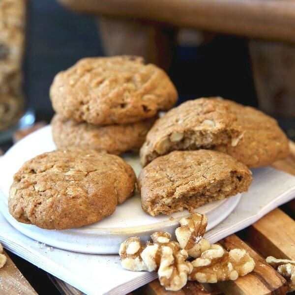 Healthier Kitchen Sink Cookies scattered 5 on a white pottery coaster and ivory colored napkins. Walnuts sprinkled around and one cookie broken open.