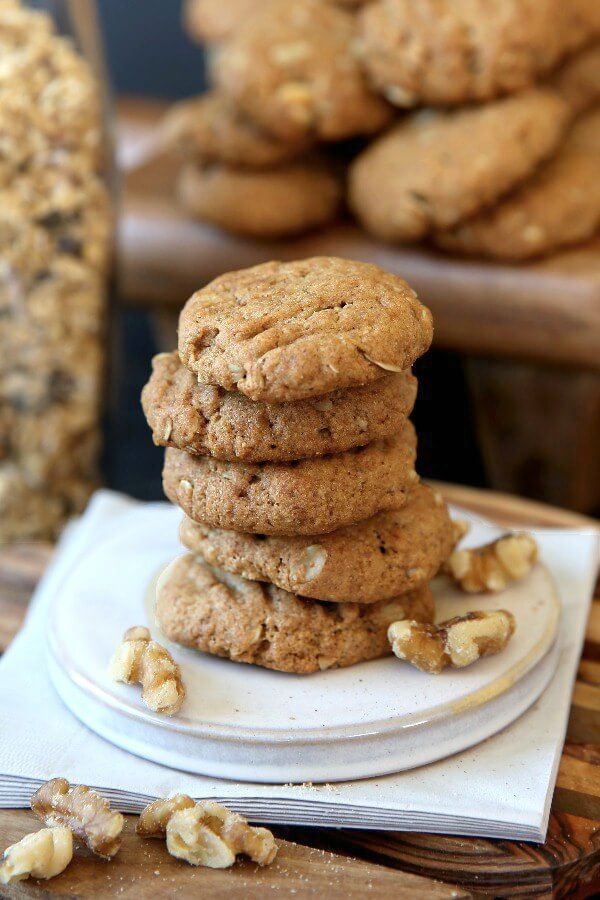 Healthier Kitchen Sink Cookies stacked 5 cookies high on a white pottery coaster and ivory colored napkins. Walnuts sprinkled around.