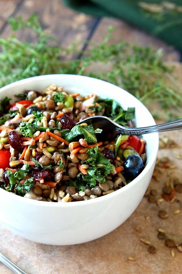 Superfood Salad with Maple Vinaigrette has every color of the rainbow in deep rich shades. It's all in a white bowl with fresh herbs in front on the granite slab with cooked lentils and rice scattered around