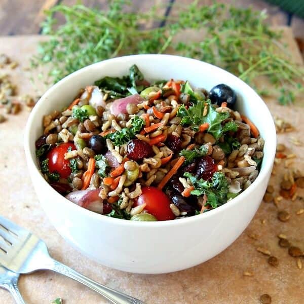 Superfood Salad with Maple Vinaigrette is in a white bowl and tilted forward so we can see eleven superfoods mixed together and glistening. Forks and herbs scattered around.