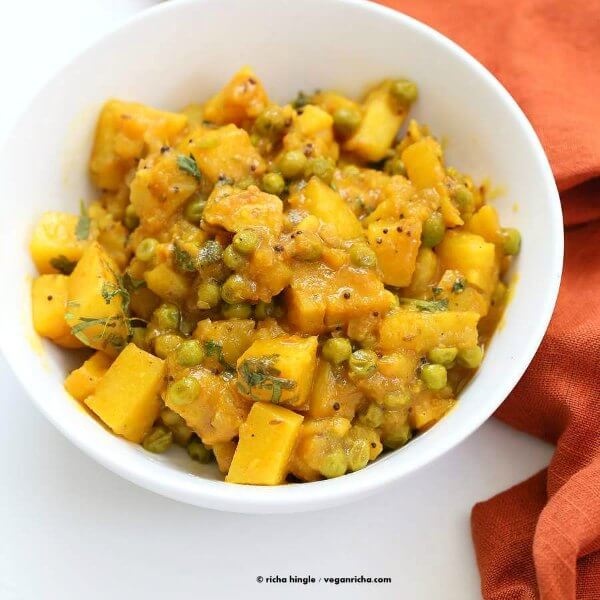 Bombay Potatoes and Peas are viewed from above and it's served in a small white bowl with an orange cloth on the side.