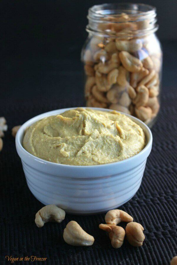 Cashew Cheddar Cheese Spread is golden and in a white rimmed bowl on black.