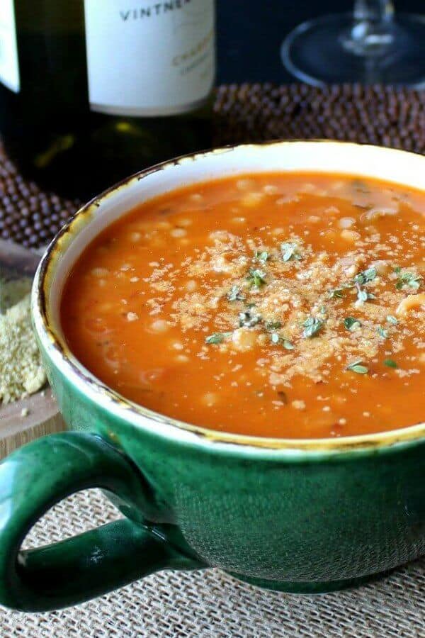 Couscous Minestrone Soup is an deep orange in color and it fills a giant green mug. Tilted forward with parmesan cheese and fresh herbs sprinkles on top.