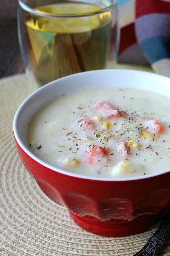 Creamy Cauliflower Soup is is in a red bowl and the creamy ivory soup is showing carrots and veggies popping through. A glass of wine is in the background.