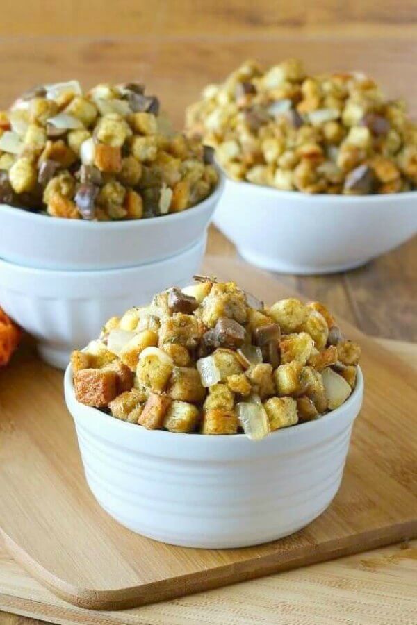 Cremini Mushroom Dressing is piled high in three different shaped white bowls and they all sit on a wooden cutting board.