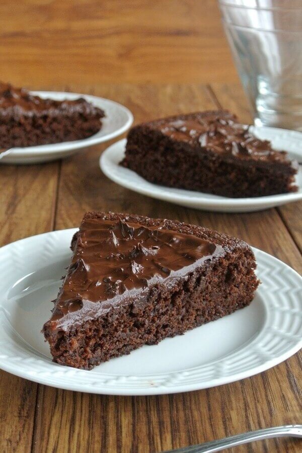 Chocolate cake has been cut into big slices and three are placed at angles in front of each other on white plates.