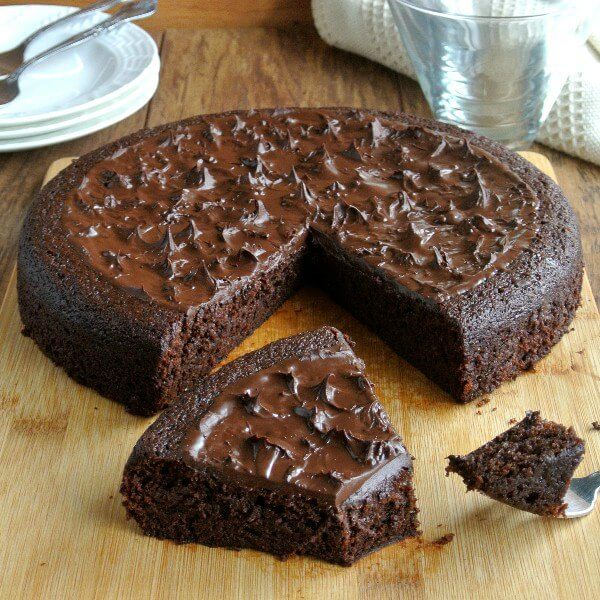 Decadent Vegan Chocolate Torte is a straight on photo of the single layer chocolate cake with one large slice cut out and placed in front of the large cake. A fork has cut off the point and it's waiting to be eaten.