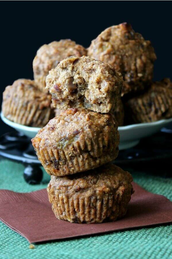 Hawaiian Banana Date Muffins are stacked three high with the top muffin torn in half to show the delicious inside ingredients. Sitting on a chocolate colored napkin and a green woven mat.