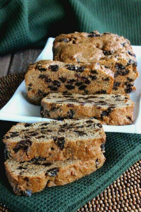 Hobo Raisin Bread is on a white plate with a few slices laying in front of the main loaf and at angles to see all the raisins inside. All on a green cloth.