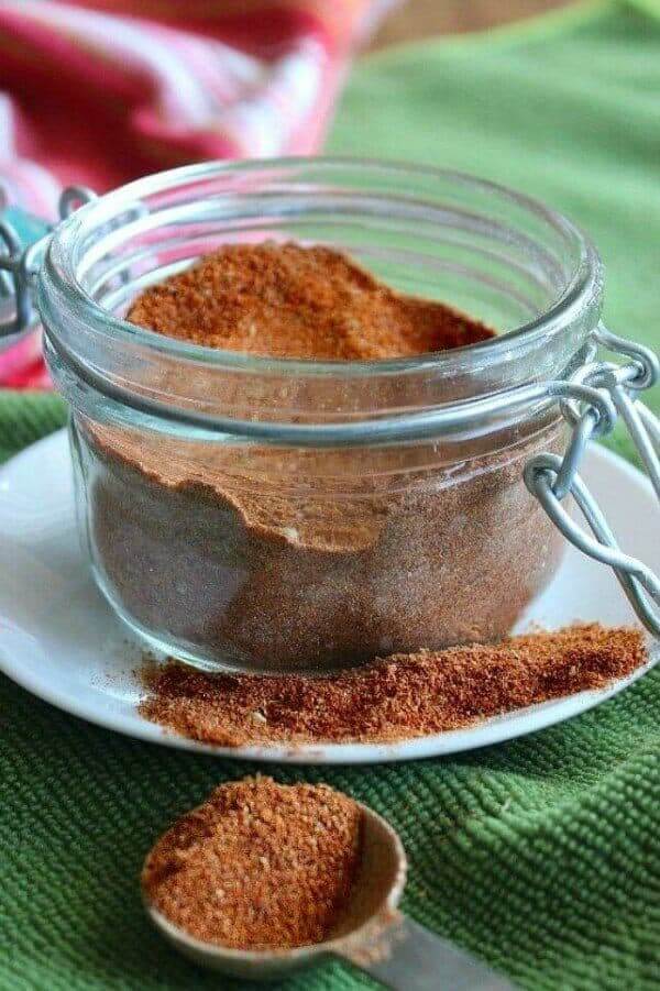 Homemade Chili Seasoning Mix is in a ½ pint jar and spilled on a white plate. A tablespoons full is sitting in front.