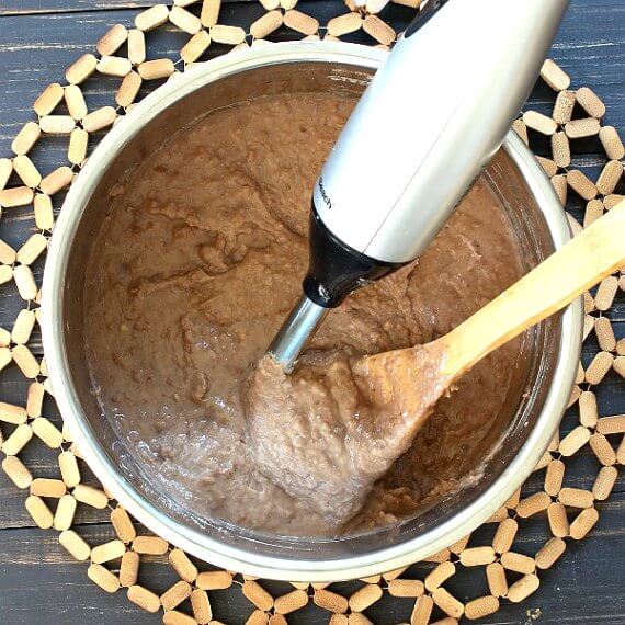 Instant Pot Refried Beans are being looked at from overhead as they have been blended in the instant pot. An immersion blender and wooden spoon are angled in the pot.