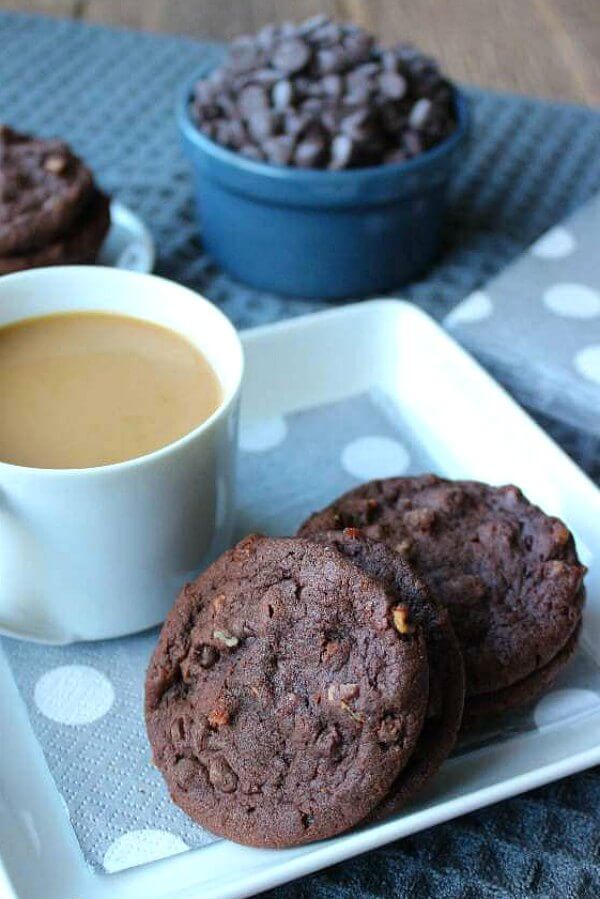 Irish Cream Chocolate Cookies are sitting on a square white plate with a cup of coffee in a white cup. Silver and silvery blue colors in the cloth and napkins.