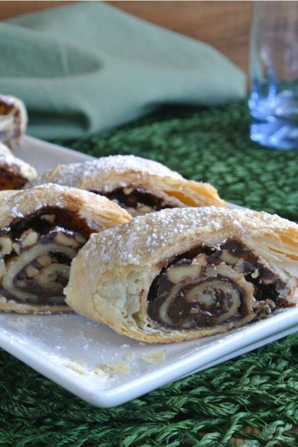 Mother's Chocolate Strudel is sliced with chocolate and walnuts showing in the rolled layers of a flaky crust. All served on a white plate.