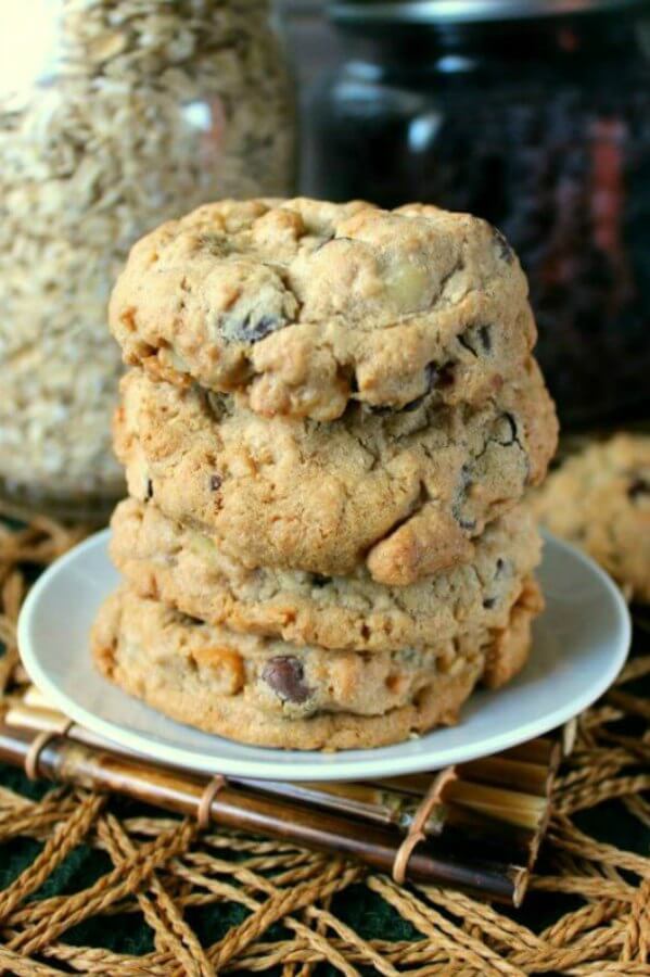 Nut Free Oatmeal Chocolate Chip Cookies are stacked 4 high and sit in small white plates sitting a an open weave beige mat.