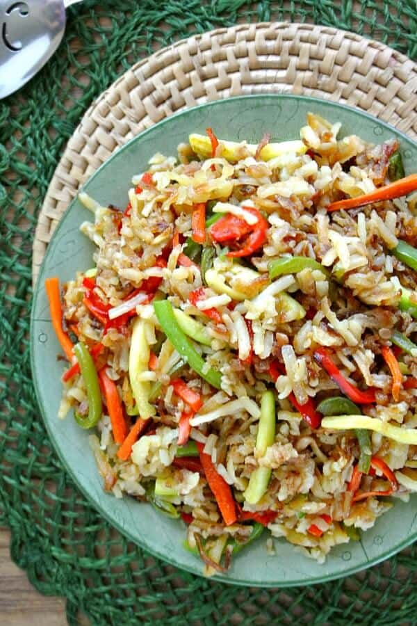 Rainbow Veggie Hashbrown Potatoes are fried together with carrots, bells, zucchini and onions. Piled high in a green and white bowl on a green mat. Overhead view and cropped in half you can see a;; of the color of the veggies mixed together.