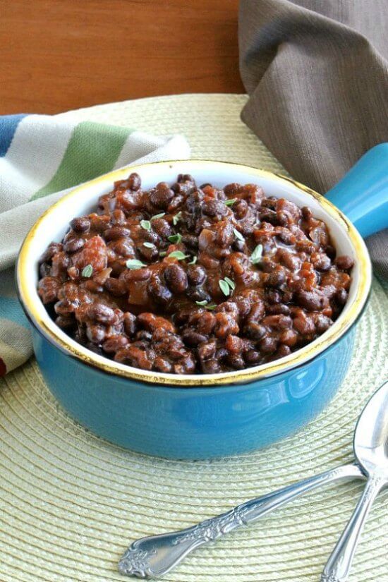 Slow Cooker Black Bean Chili is in a bright turquoise bowl and is tilted towards the camera. Ste on an ivory mat with two spoons on the side.