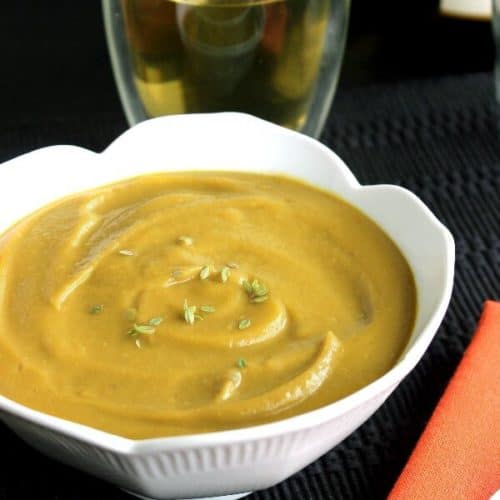 Vegan Split Pea Soup is bright golden in a white scalloped bowl against a black placemat.