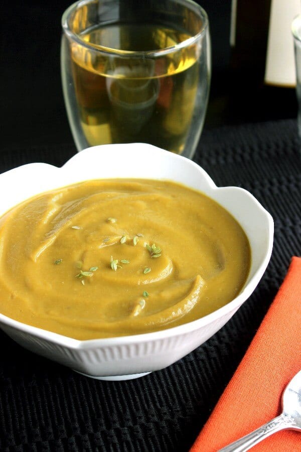 Vegan Split Pea Soup is bright golden in a white scalloped bowl against a black placemat.