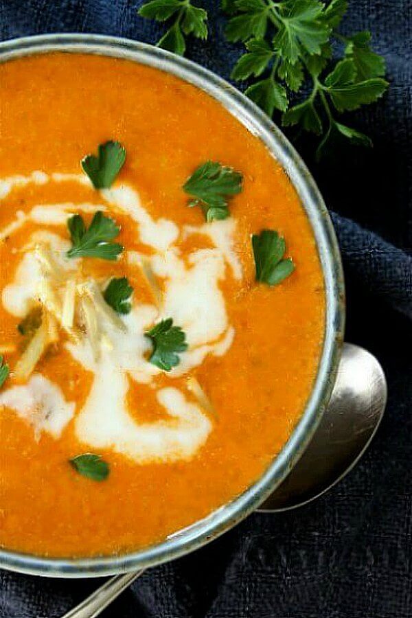 Cauliflower Tikka Masala Soup is a warm orange color and is in a silver bowl and garnished with a swirl of cream and fresh parsley.