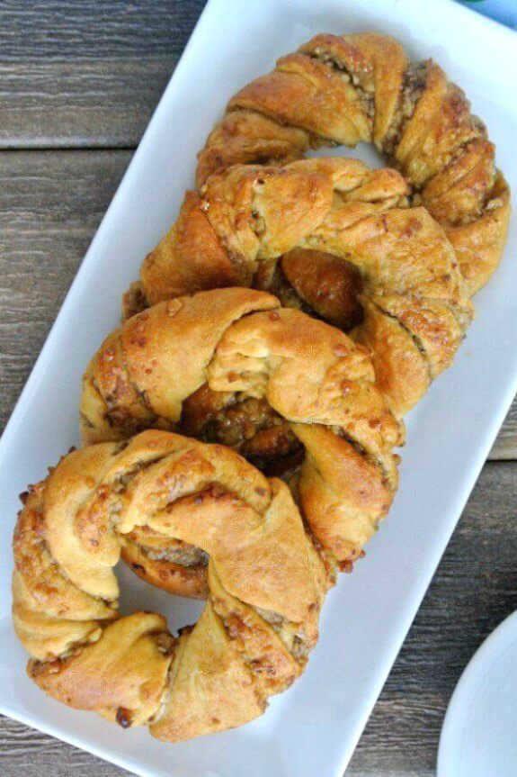 Crescent Roll Breakfast Rings sprawled down a rectangle white plate. 5 Rings are overlaying each other and glistening with sweetness.