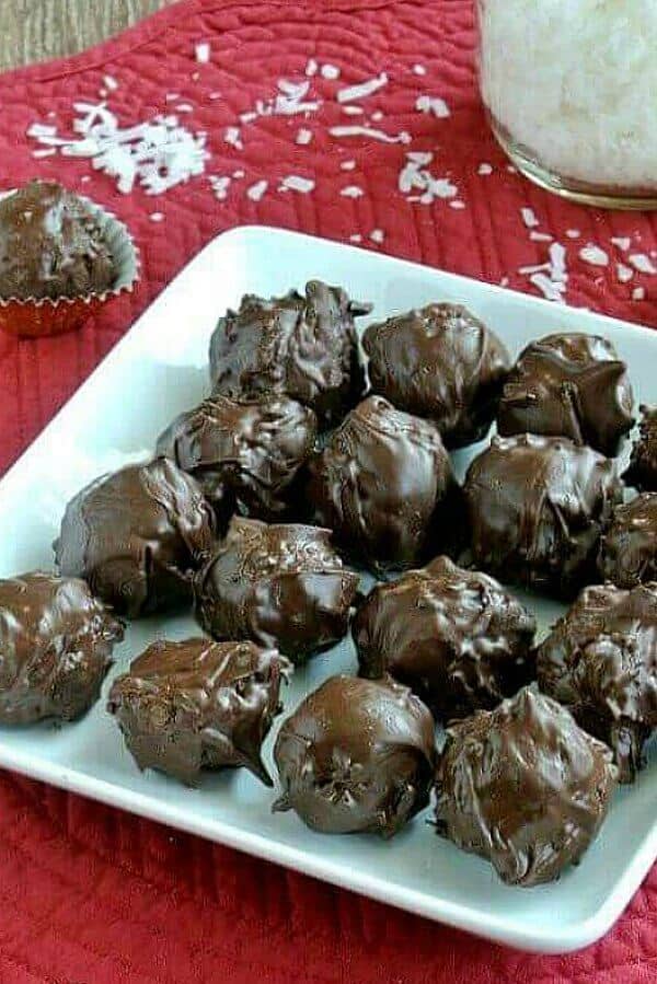 Copycat Chocolate Mounds Candy is lined up straight 4 x 4 on a white square plate and set against a red mat.